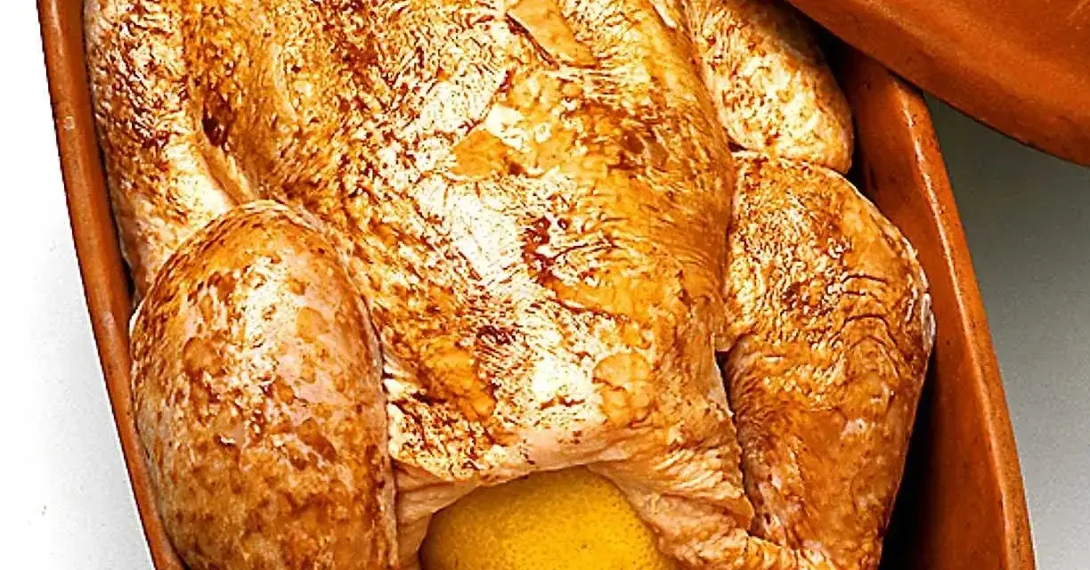 En hel kyckling med gyllene skinn och en citron i magen, redo att tillagas i en lergryta.