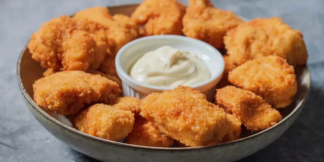 En skål med gyllene, krispiga chicken nuggets och en liten skål med krämig dipp. Perfekt för en snabb och god måltid.