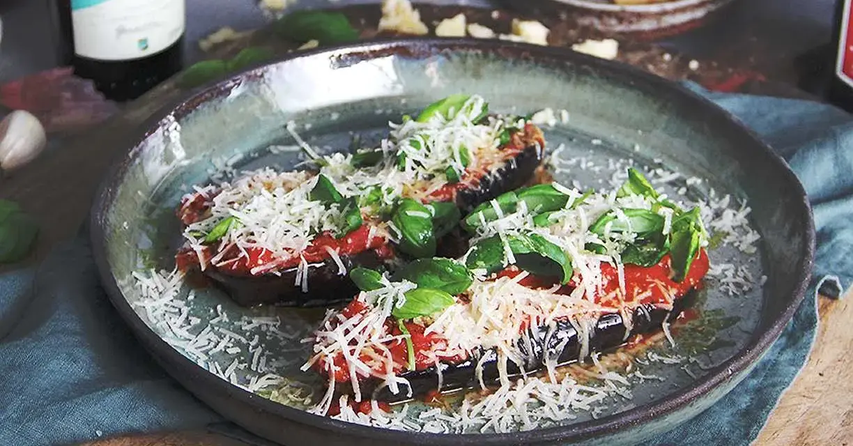 Halverade auberginer toppade med tomatsås, basilika och riven ost, redo att tillagas i ugnen. En härlig aubergine i ugn.