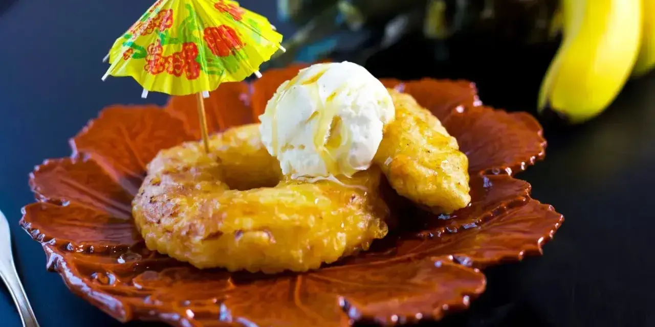 Friterad banan med vaniljglass och en liten gul parasoll. En tropisk dessert som smakar sommar.