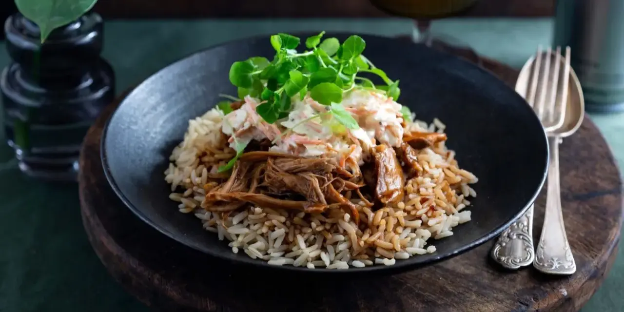 En tallrik med pulled pork med ris, toppad med krispig coleslaw och gröna blad. En härlig måltid som ser utsökt ut.