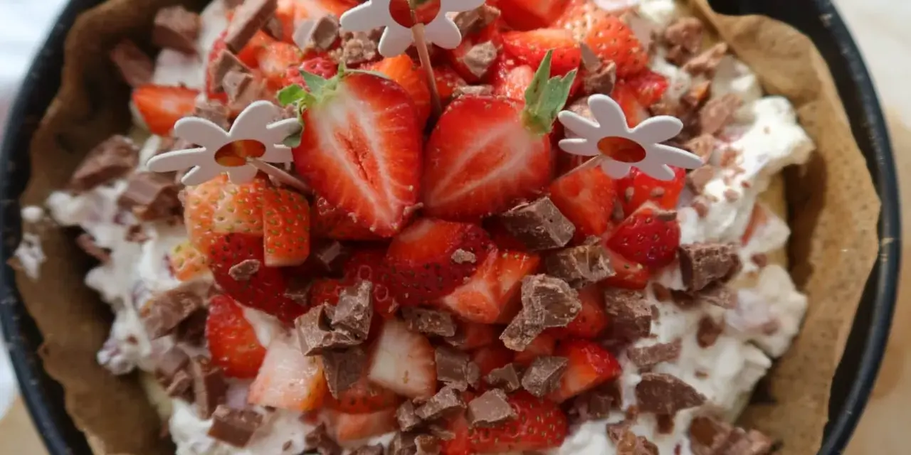 En läcker cheesecake med jordgubbar och chokladbitar, perfekt för ett somrigt cheesecake recept. Blomsterpinnar dekorerar toppen.