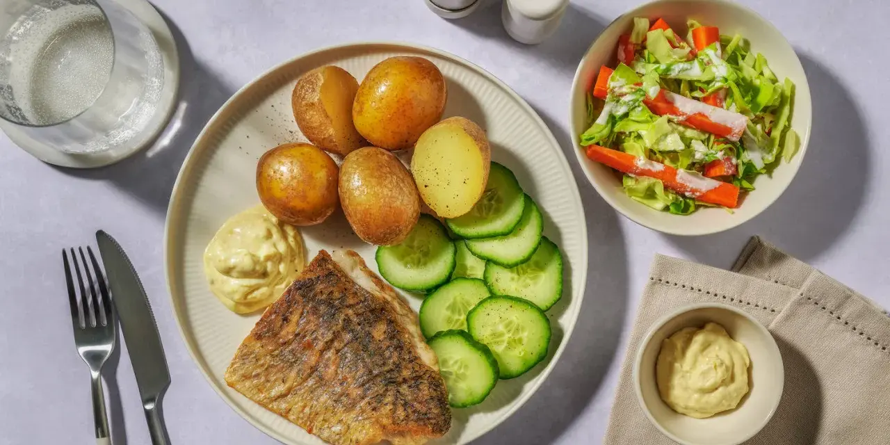 En tallrik med stekt vit fisk, kokt potatis, gurka och en klick majonnäs. Ett perfekt vit fisk recept för en snabb middag.