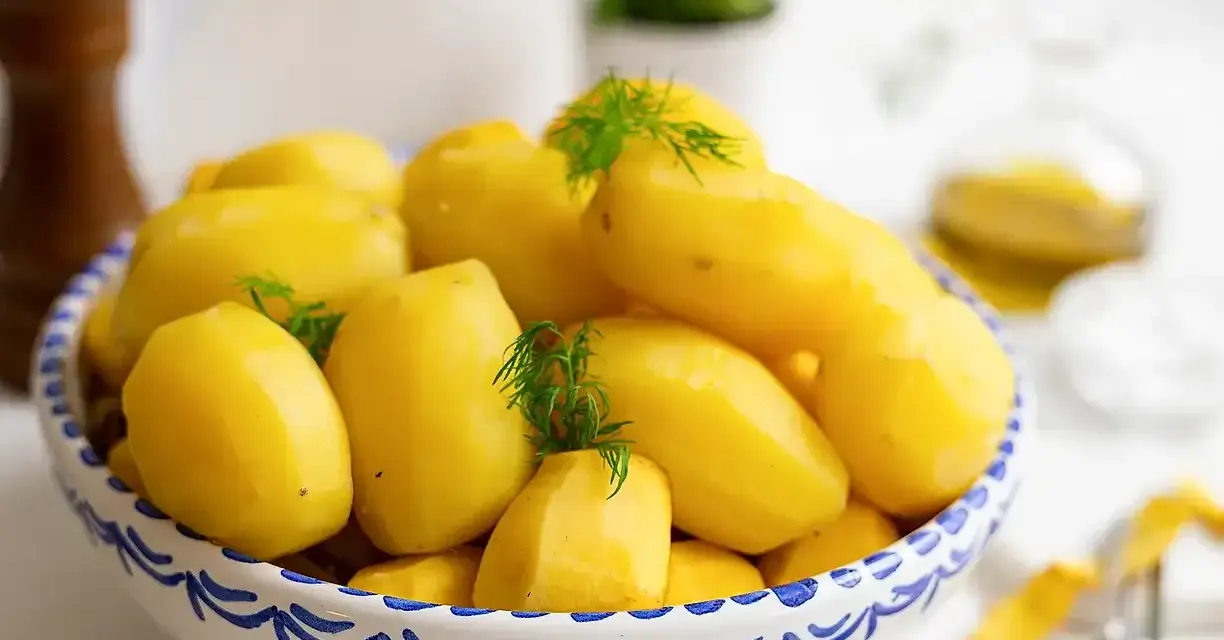 Nyskållade, gula potatisar i en blåvit skål, redo att koka. Dillkvistar ger en fräsch touch.
