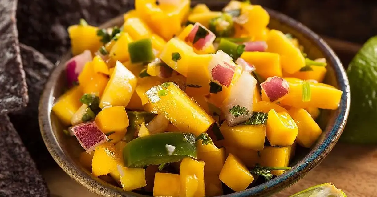 En skål med färgglad mango salsa, med tärnad mango, rödlök, grön paprika och koriander. Serveras med tortillachips och limeklyftor.