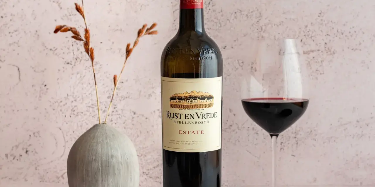 En flaska Rust en Vrede Estate vin, perfekt till oxfilé, står bredvid ett glas rött vin och en liten skål med pepparkorn.