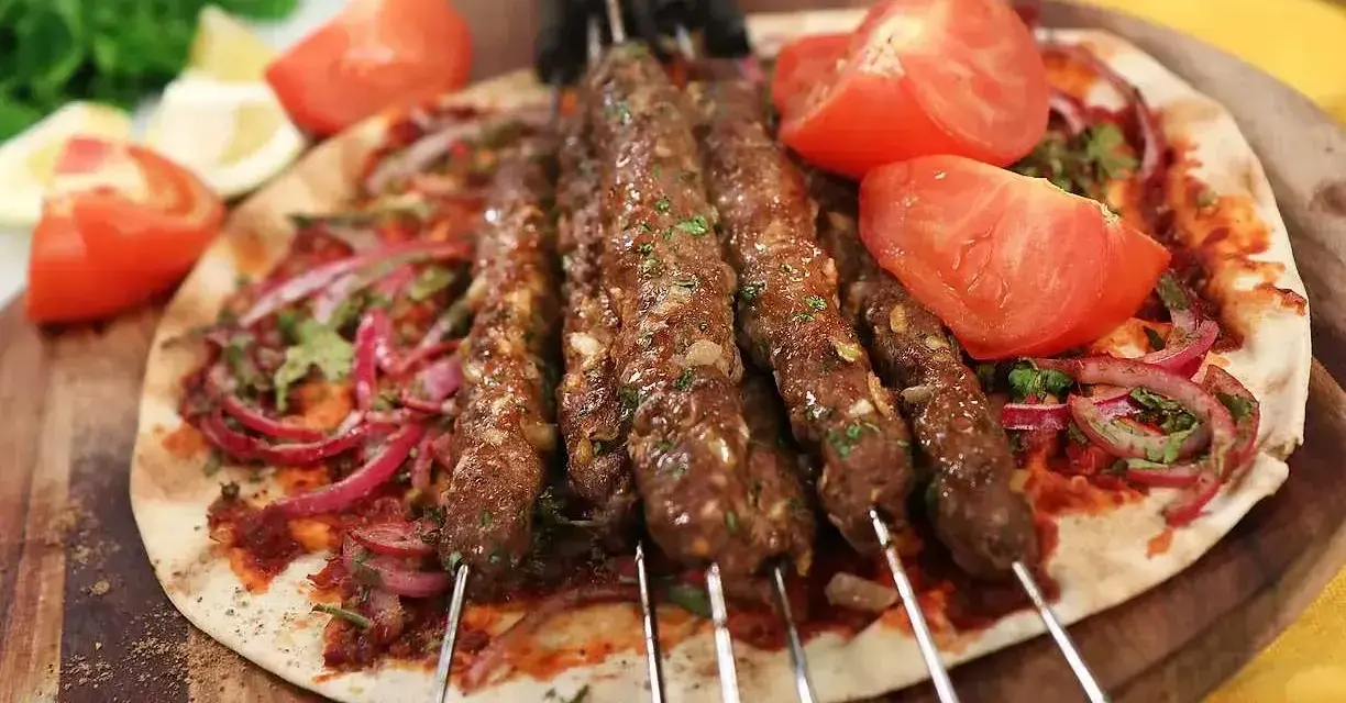 Grillade Adana kebabspett på en bädd av tunnbröd med rödlök, tomat och persilja. Ett perfekt adana kebab recept för en smakrik måltid.