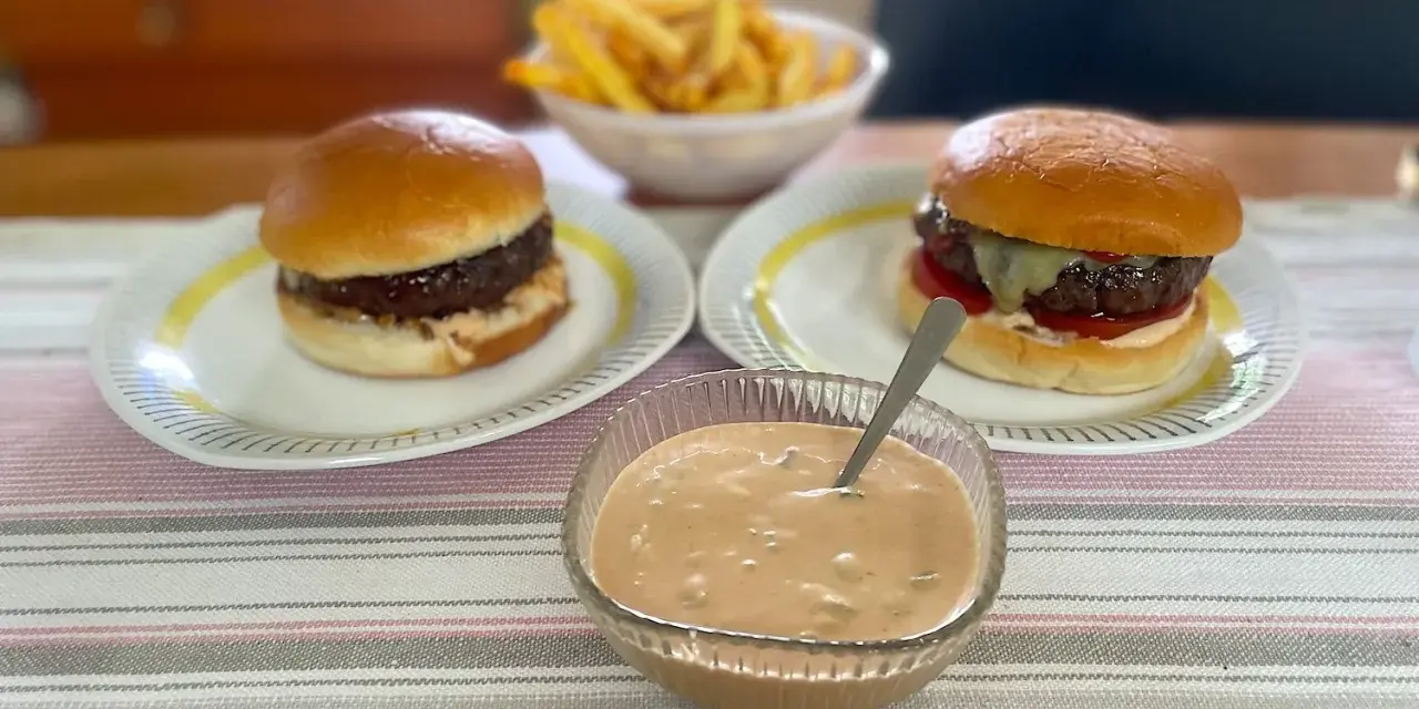Två hamburgare med pommes frites och en skål med hemlagad hamburgerdressing. Perfekt för en mysig hemmakväll!