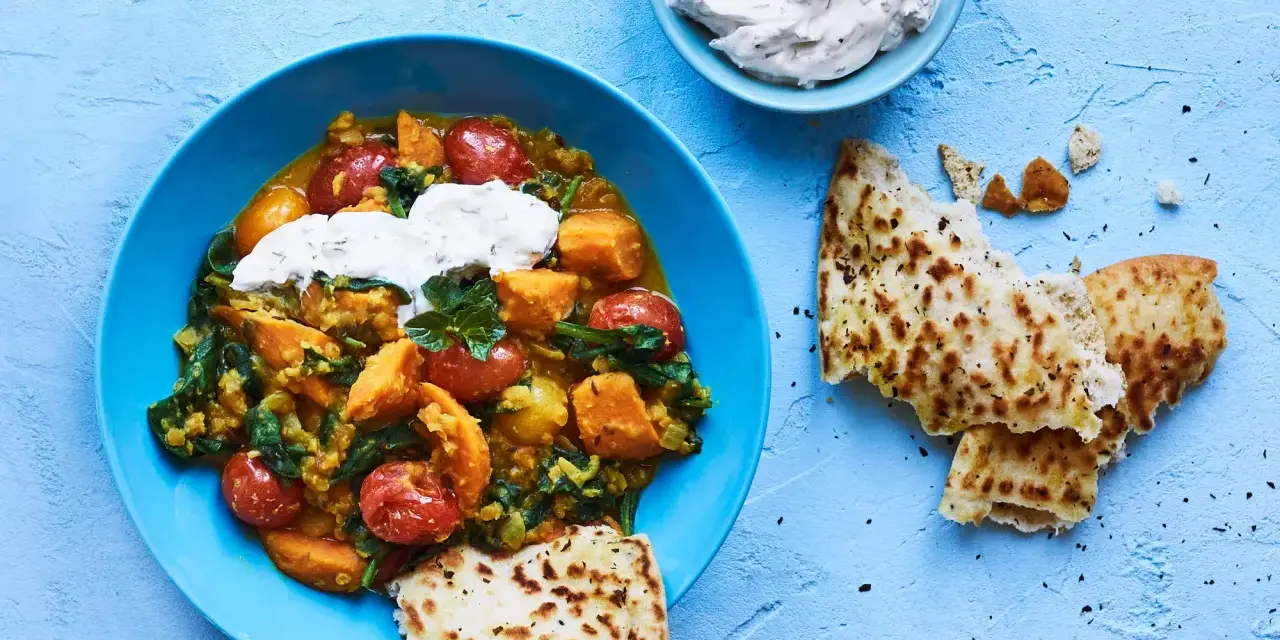 En blå skål med en mustig daal med sötpotatis, spenat och tomater, toppad med gräddfil. Serveras med naanbröd.