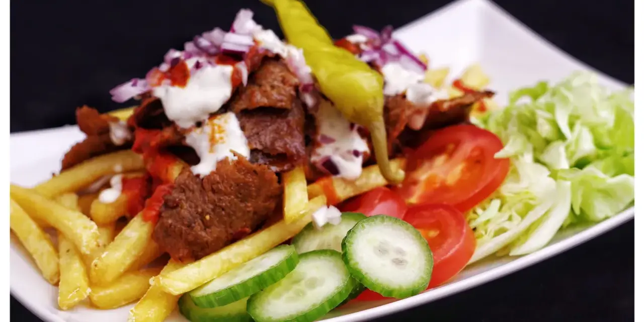 En tallrik med kebab, pommes frites, tomater, gurka, sallad och en grön chili. Perfekt för att inspireras till ett gott kebabsås recept.