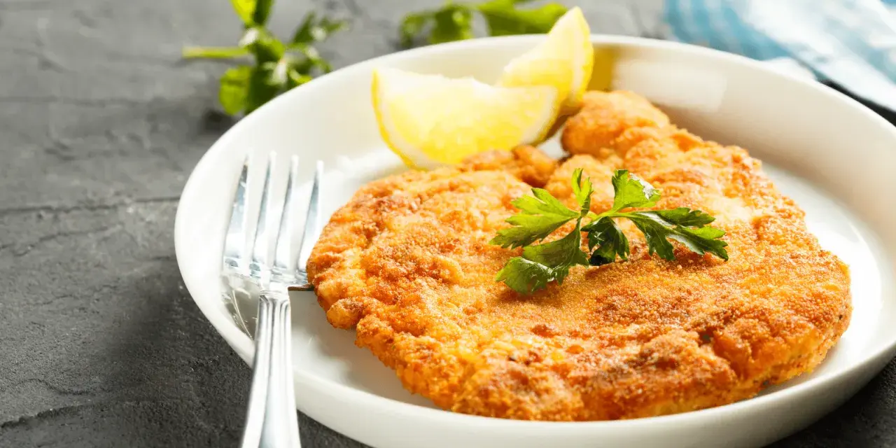 En gyllene schnitzel med citronklyfta och persilja, redo att avnjutas med ett glas vin till schnitzel.