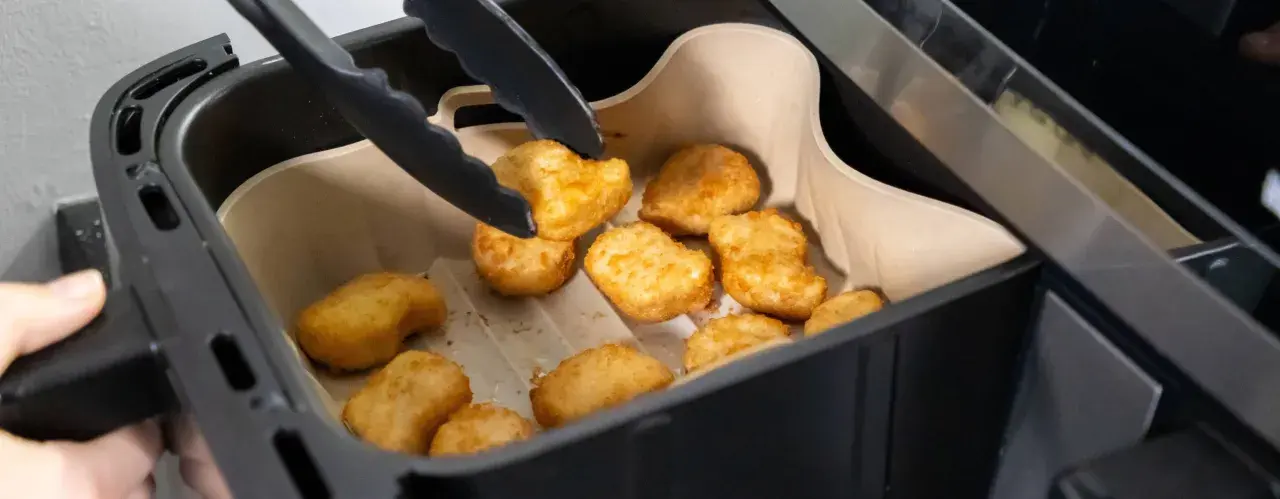 Tång tar upp gyllene, krispiga tater tots ur en airfryer.
