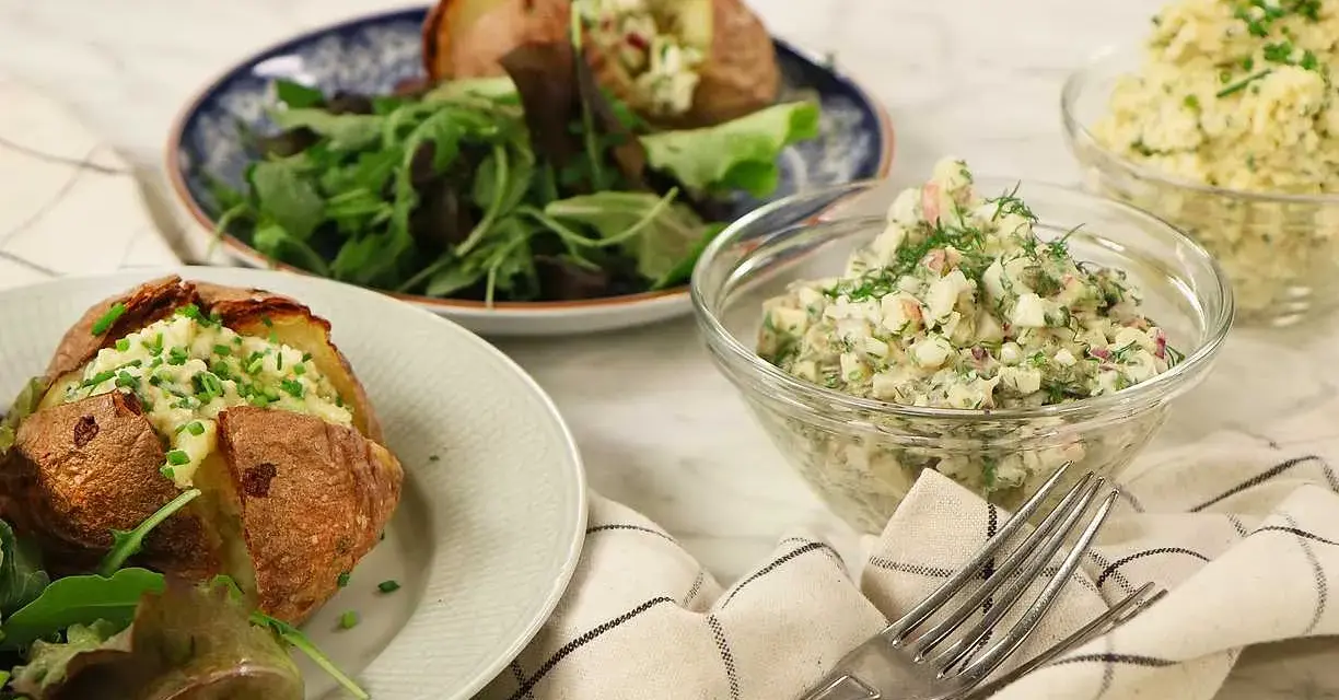 Två bakade potatisar med en krämig bakad potatis fyllning, serverade med en fräsch sallad och två skålar med olika röror.