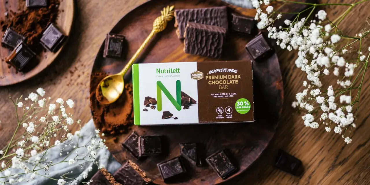 Chokladbitar och en förpackning med Nutrilett Premium Dark Chocolate Bar, en del av deras kalorisnål mat-sortiment.