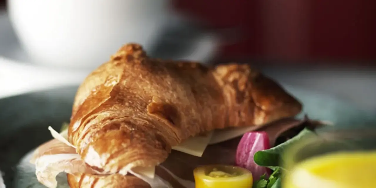 En gyllene croissant fylld med skinka och ost, serverad med grönsaker och juice. Perfekt för en snabb frukost eller lunch, som ett enkelt croissant recept.