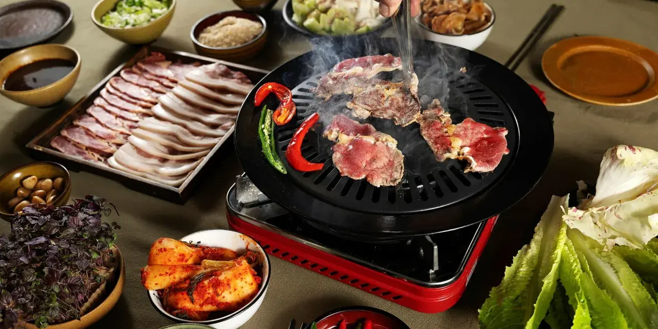 En härlig **korean bbq**-upplevelse med saftigt kött som grillas, serverat med kimchi, vitlök och färska grönsaker.