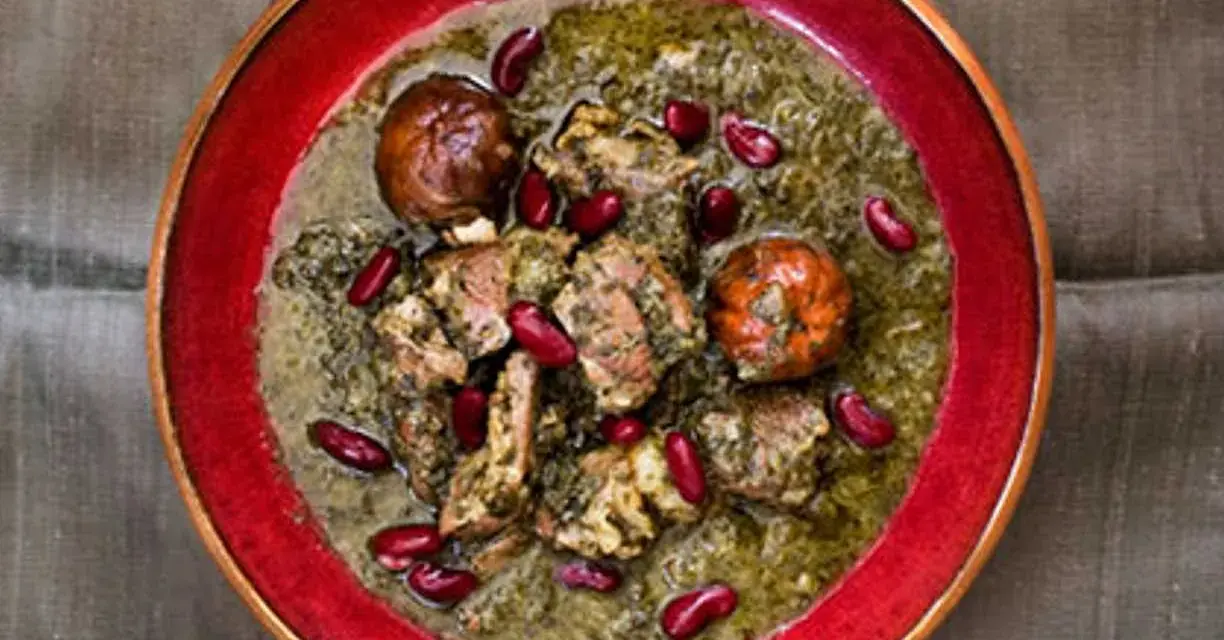 En skål med ghorme sabzi, en mustig persisk gryta med kött, örter och röda bönor, serverad i en röd kantad skål.