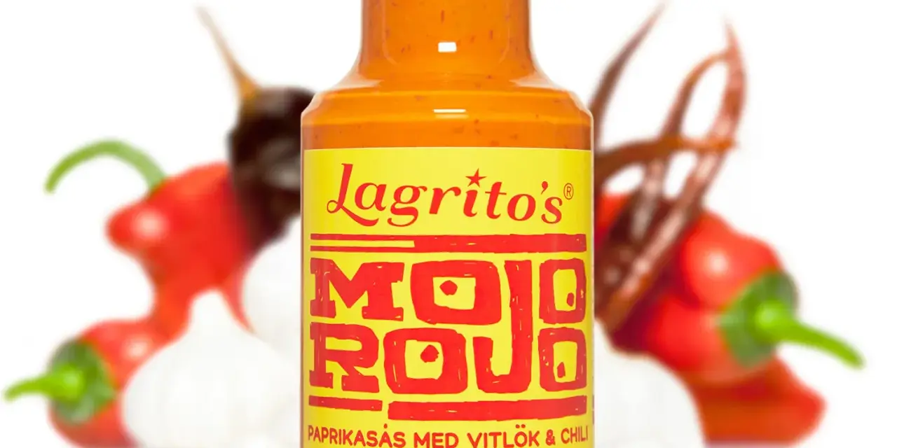 En flaska Lagrito's Mojo Rojo, en paprikasås med vitlök och chili, omgiven av färska chilis och vitlök.