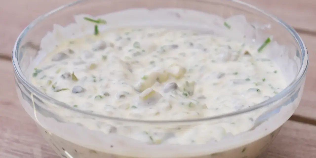 En krämig kall sås till fisk, med kapris och örter, serverad i en glasskål på en träyta.