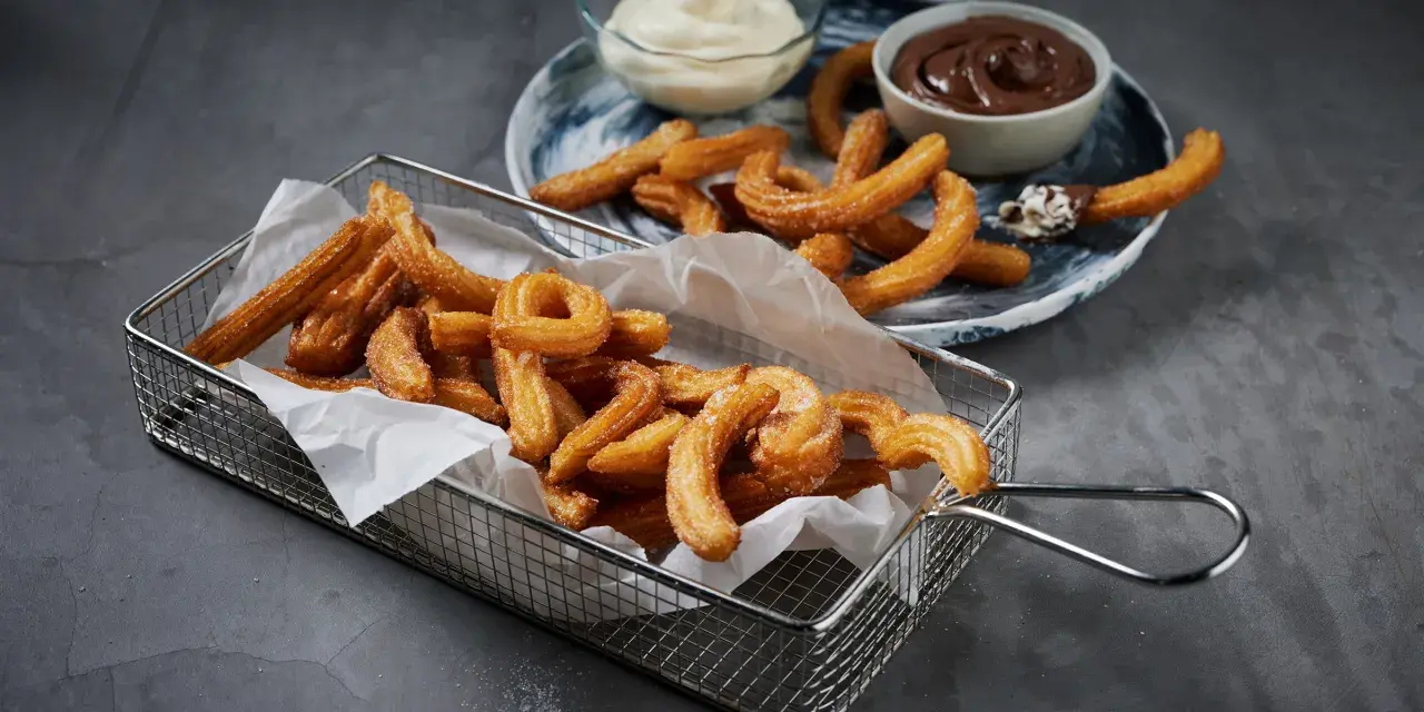 Krispiga churros i korg med chokladsås och grädde. Perfekt för ett enkelt churros recept hemma.