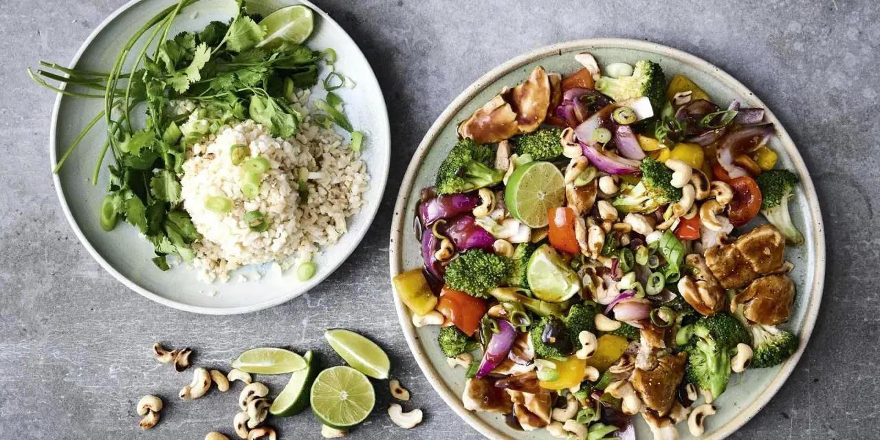 Två tallrikar med mat. En med ris, koriander och salladslök. Den andra med kyckling, broccoli, paprika, cashewnötter och lime. Perfekt för nyttiga recept.