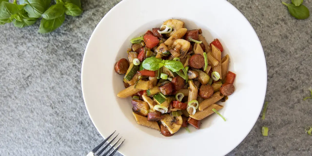 En tallrik med chorizo pasta med grönsaker som paprika, zucchini och champinjoner. Garnerad med färsk basilika och salladslök.