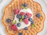 En vacker, blomformad våffla toppad med vispgrädde, hallon och blåbär. Perfekt för en fika med glutenfria våfflor.