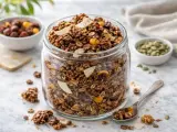En stor burk fylld med hemgjord granola, perfekt för ett hälsosamt frukostrecept. Nötter, frön och torkad frukt syns tydligt.