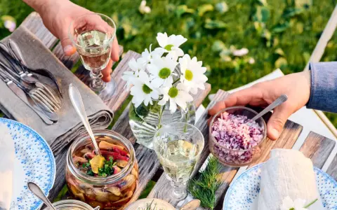 En härlig sommarmåltid med inlagd sill, hackad rödlök och vitt vin till sillen. Blommor och grönska i bakgrunden.