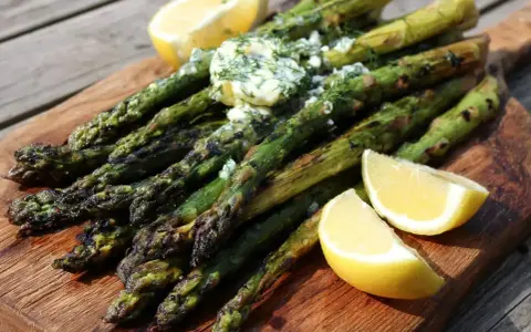Grilla sparris med smör och dill, serverad med citronklyftor på en träskärbräda. Perfekt sommarbuffé!