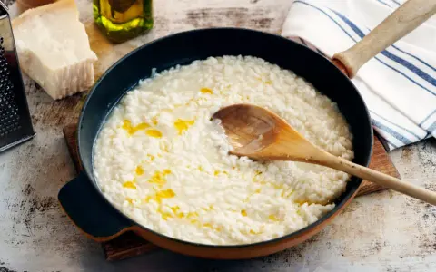 Krämig risotto i panna, med parmesan, olivolja och en träsked. Perfekt för ett enkelt risotto recept.