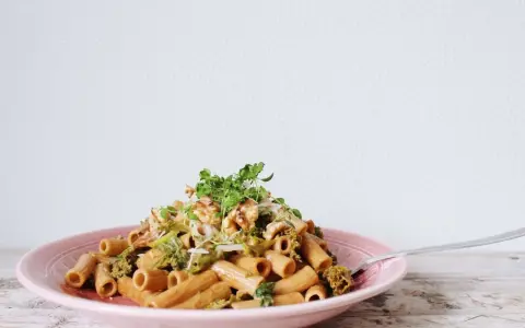 En läcker vegetarisk pasta med broccoli, valnötter och färska örter på en rosa tallrik.