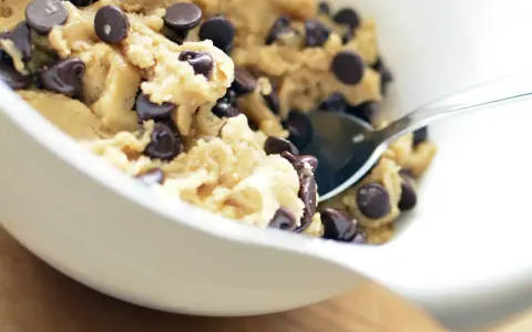 En skål med ljuvlig cookie dough med chokladbitar, redo för ett enkelt cookie dough recept. En sked vilar i smeten.