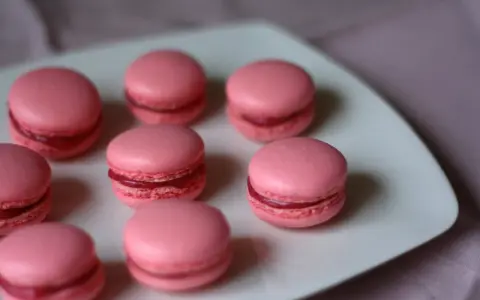 Rosa macarons med hallonfyllning på en vit tallrik. Perfekt för ett macarons recept.