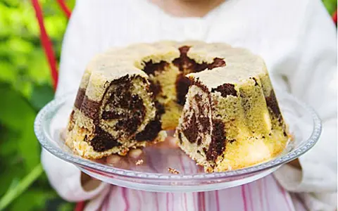 En barn håller upp en marmorerad tigerkaka på ett fat. Ett perfekt tigerkaka recept för fikat.