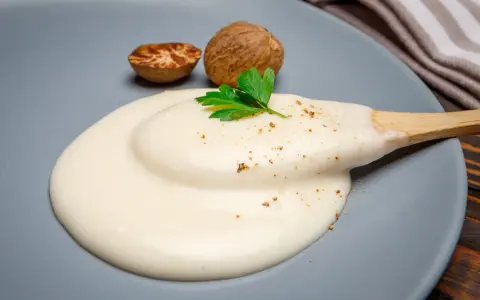 Krämig bechamelsås på en tallrik med muskotnötter och persilja. Ett perfekt bechamelsås recept för alla tillfällen.