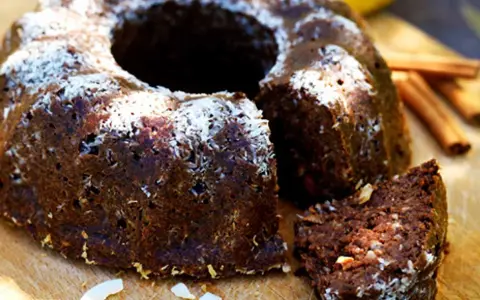 En saftig banankaka med choklad, toppad med kokosflingor. En bit är uppskuren och visar den rika, mörka insidan.