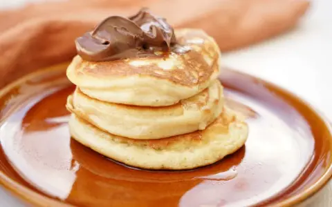 Stack of three fluffy American pancakes topped with chocolate spread on a brown plate.
