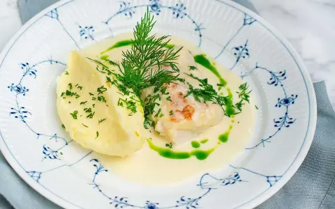 En vacker tallrik med torskrygg recept, serverad med krämigt potatismos och en grön dillolja.