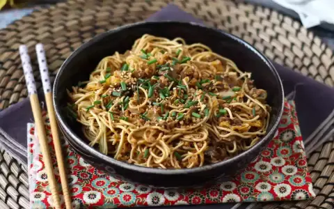 En skål med nudlar, köttfärs och grönsaker, toppad med sesamfrön och gräslök. Ett perfekt wok recept för en snabb middag.