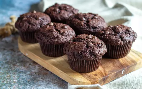 Fem saftiga chokladmuffins med chokladknappar på en träbricka. Perfekt för ett chokladmuffins recept.