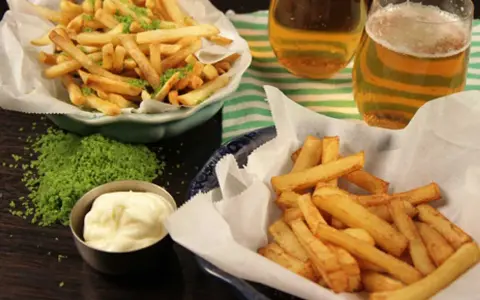 Två skålar med krispiga pommes frites, en med grön kryddning, bredvid två glas öl och en skål majonnäs.