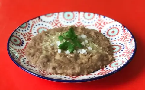 En tallrik med refried beans, toppad med lök och persilja. Ett enkelt och gott refried beans recept.
