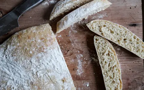 En hel och skivad ciabatta på en träskärbräda, redo för ett gott ciabatta recept. Mjöl strött över.