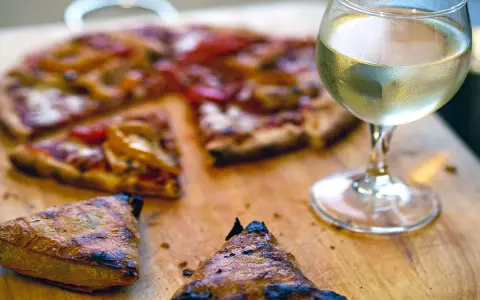 En skiva pizza med ett glas vitt vin. Perfekt vin till pizza för en mysig kväll.