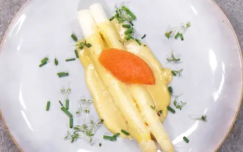 Vit sparris med krämig hollandaisesås, toppad med rom och garnerad med gräslök och örter. En klassisk och elegant rätt.
