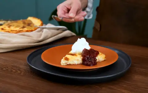 En bit krämig ostkaka med sylt och grädde, redo att avnjutas. Ett perfekt ostkaka recept för fikat.