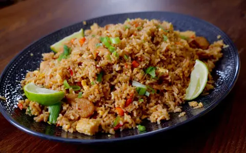 En tallrik med utsökt fried rice, garnerad med limeklyftor och salladslök.
