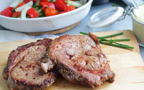 Två saftiga entrecôte-biffar på skärbräda, redo för ett utsökt entrecote recept. Grönsaker i bakgrunden.