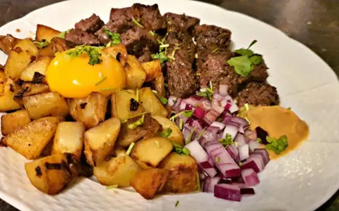 En tallrik med biff Rydberg: tärnad biff, stekt potatis, rå äggula, hackad rödlök och en klick sås. Perfekt vin till biff rydberg!